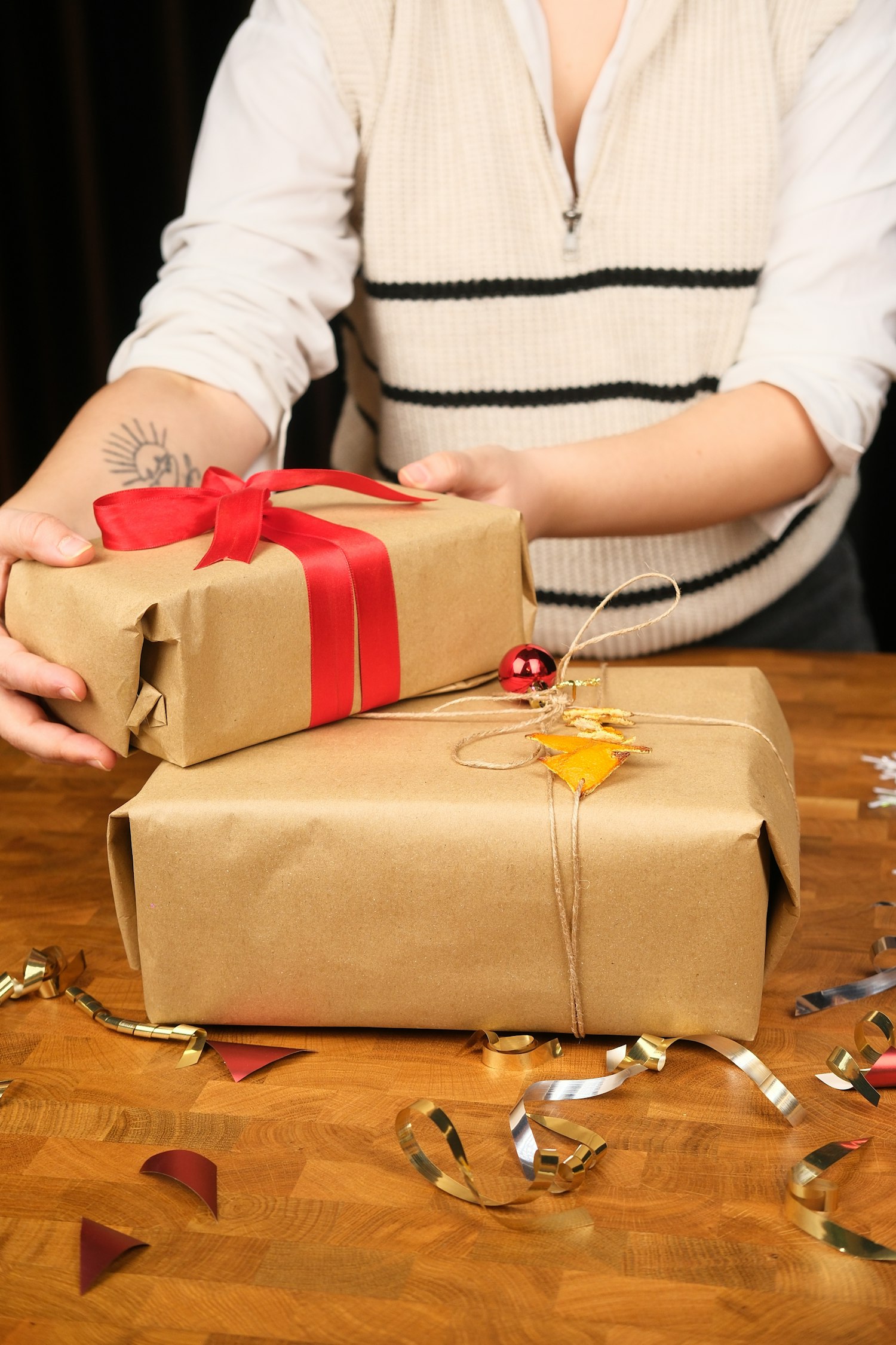 Hands wrapping a gift in kraft paper with red ribbon