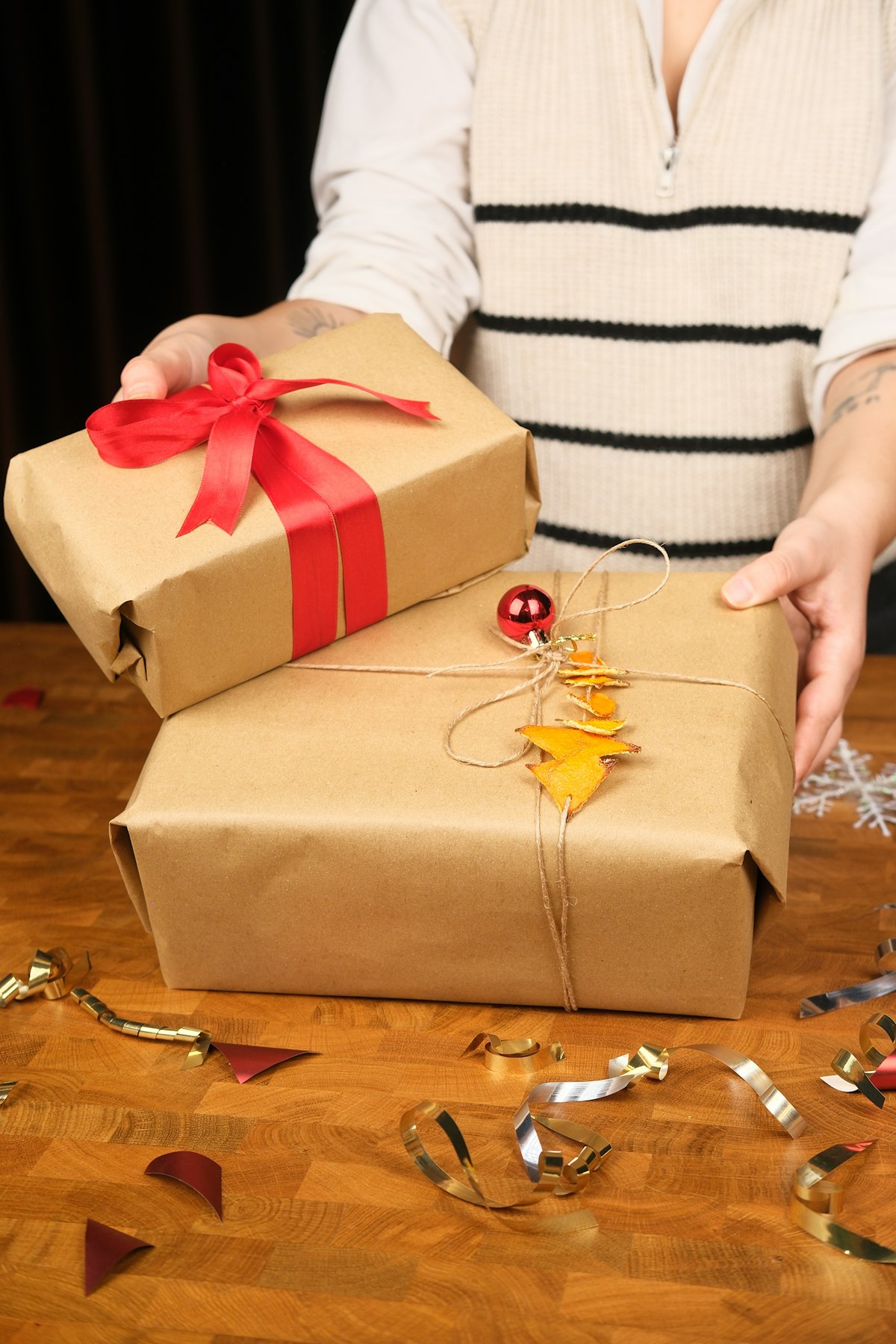 Hands holding two wrapped gifts with red ribbon